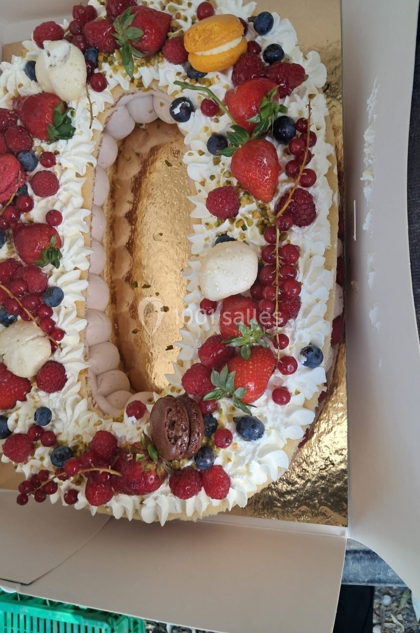 Gâteau en forme de chiffre décoré de fruits rouges, macarons et crème chantilly sur un plateau doré.