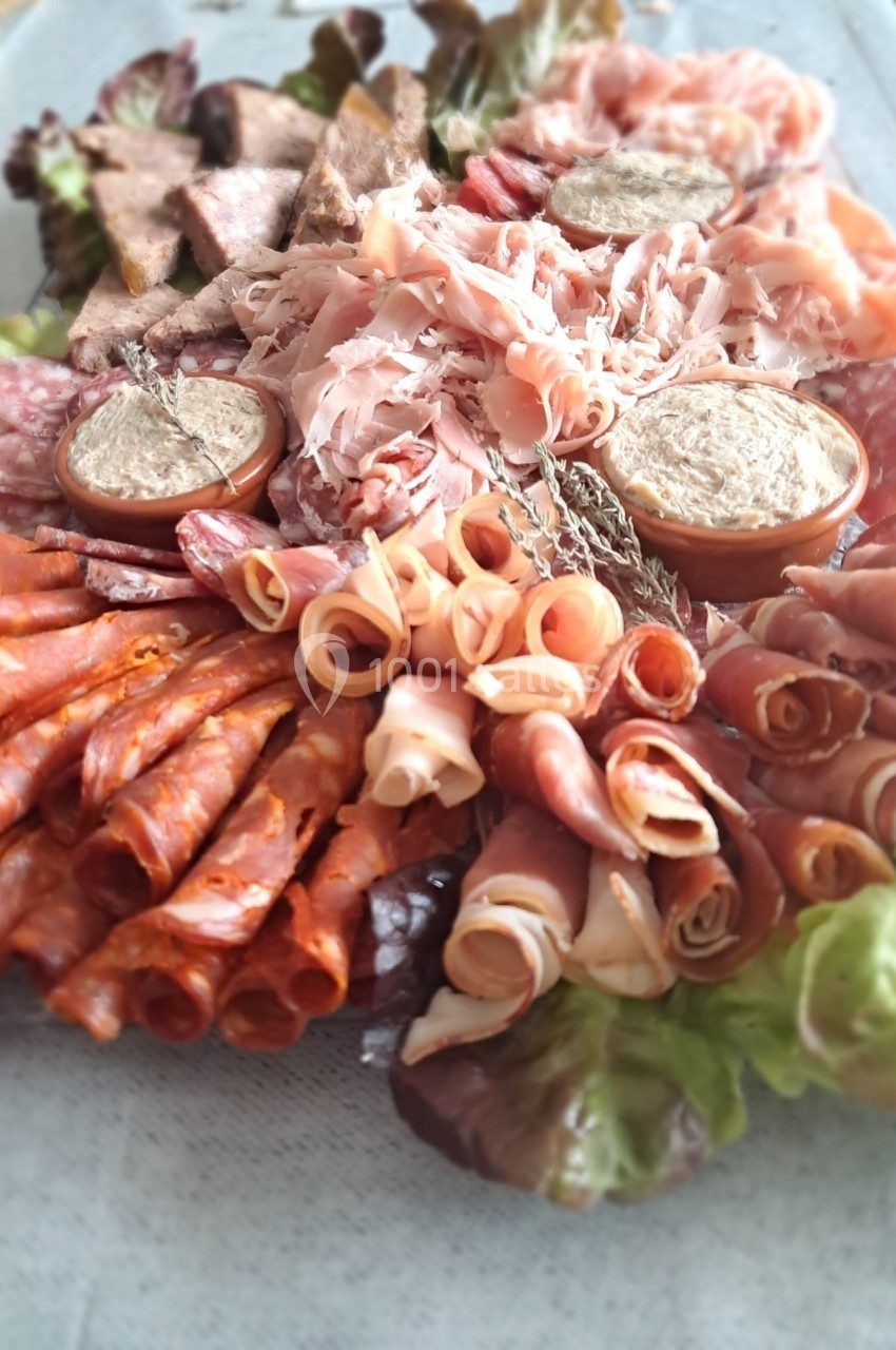 Plateau de charcuterie variée avec jambon, saucisson, pâté et feuilles de salade en décoration.