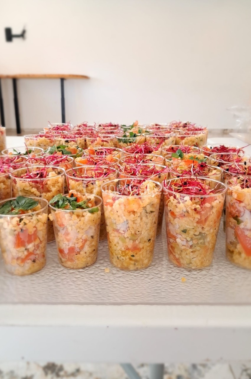 Verrines remplies de salade de lentilles corail, tomates, herbes fraîches et pousses colorées, disposées sur une table…