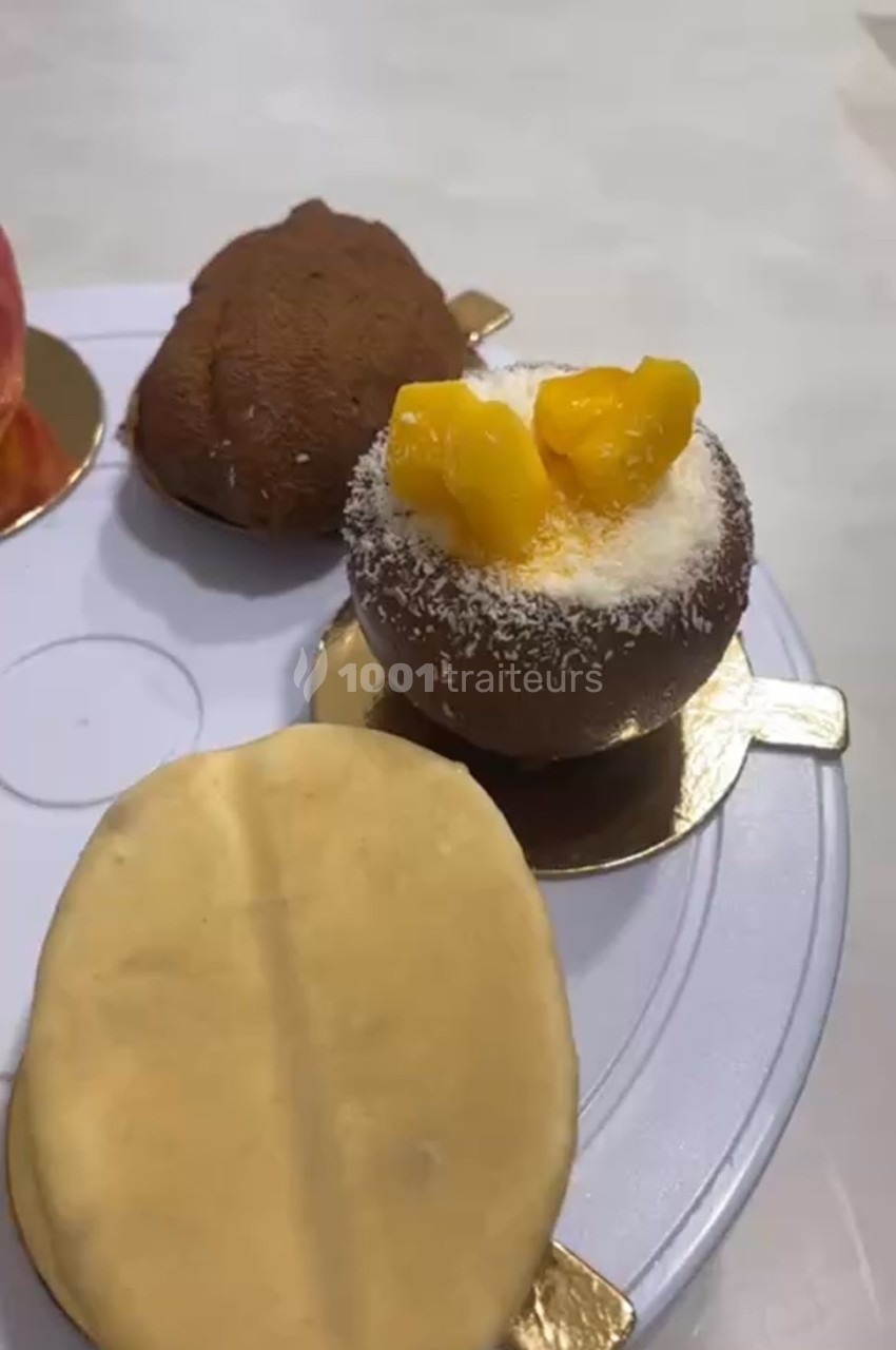 Assortiment de pâtisseries sur un plateau, dont une garnie de morceaux de fruits jaunes et saupoudrée de noix de coco.