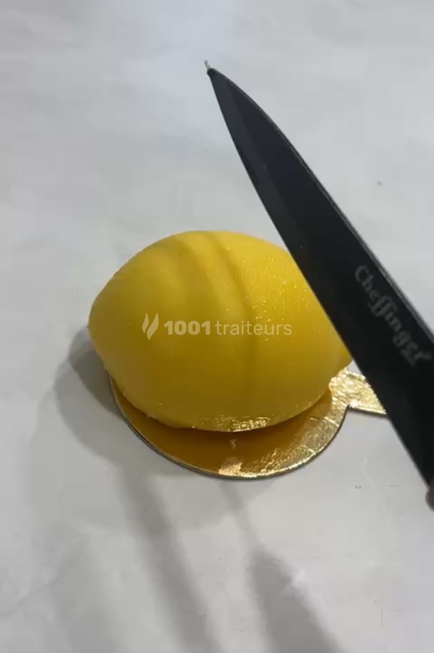 Un couteau s'apprête à couper un dessert en forme de citron posé sur un support doré.