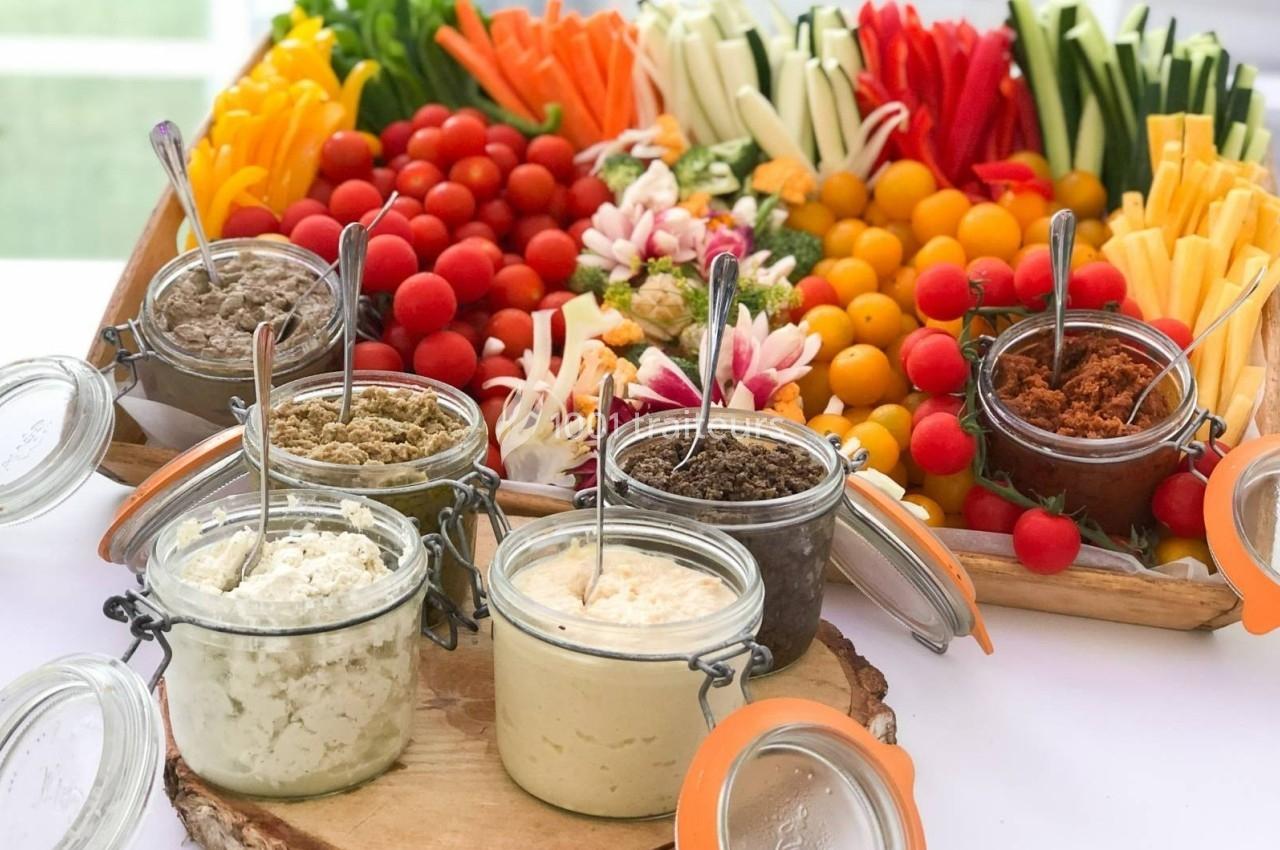 Plateau de légumes colorés avec des bâtonnets de crudités et des tomates cerises, accompagnés de plusieurs sauces en pots.