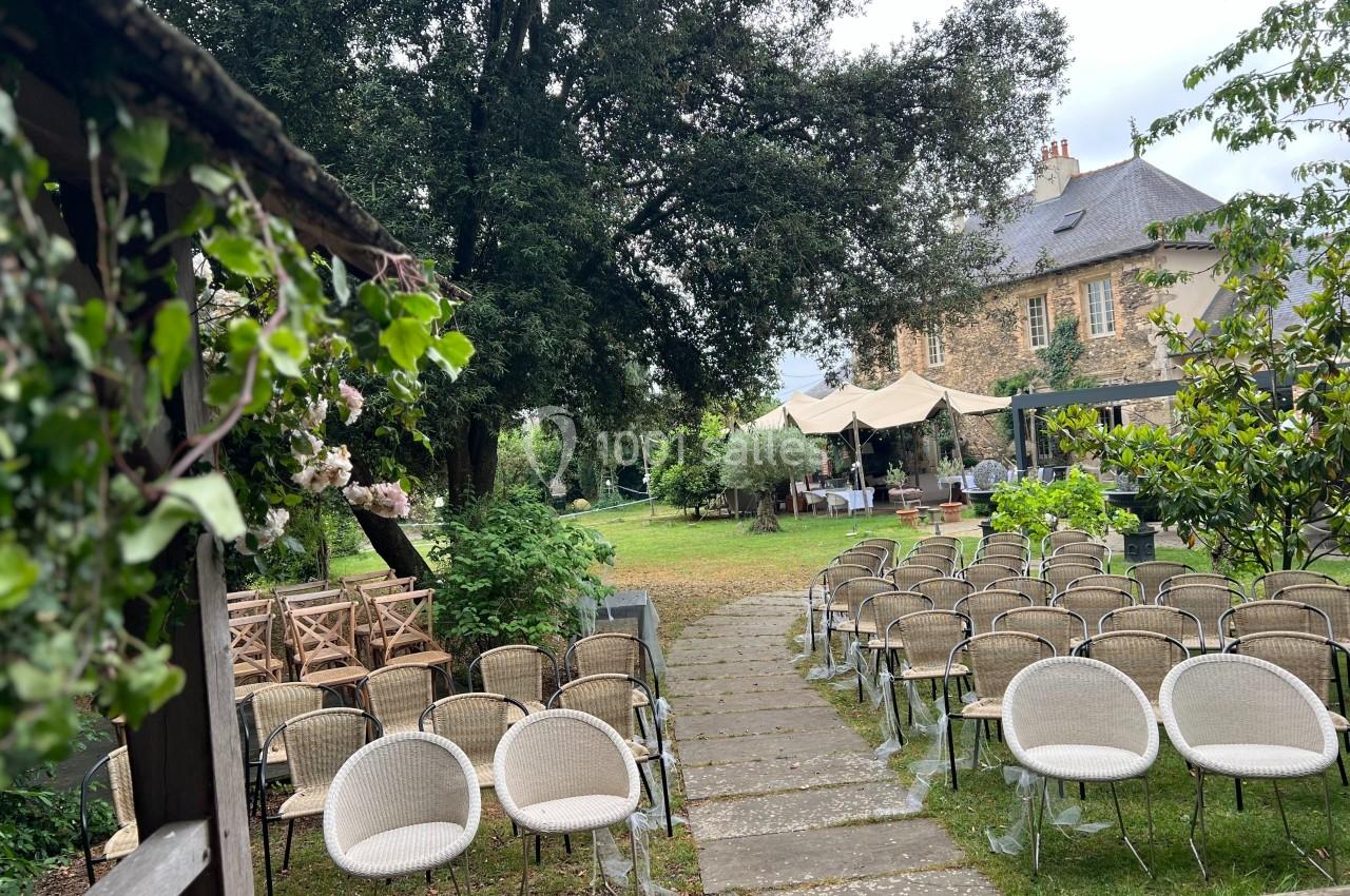 Chaises disposées en extérieur devant une maison en pierre, avec un jardin verdoyant et des arbres en arrière-plan.