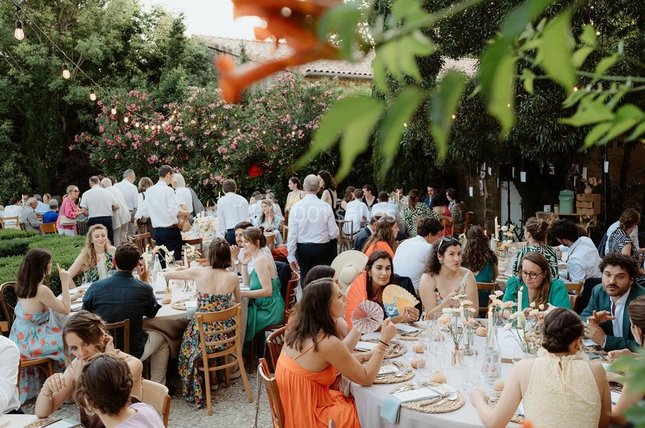 Des convives assis à des tables décorées, partageant un repas en extérieur sous des guirlandes lumineuses.
