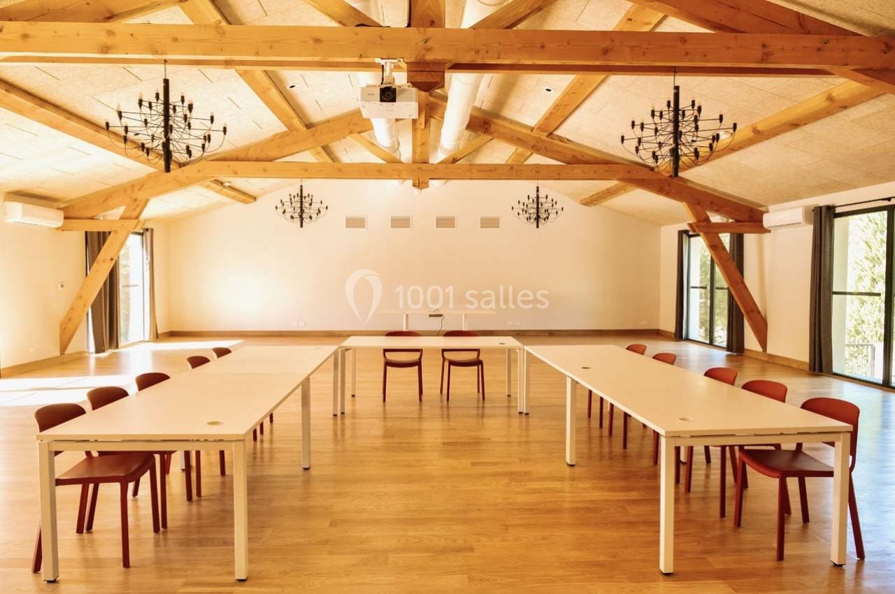 Salle lumineuse avec poutres apparentes, tables blanches disposées en U et chaises rouges, éclairée par des lustres et des…