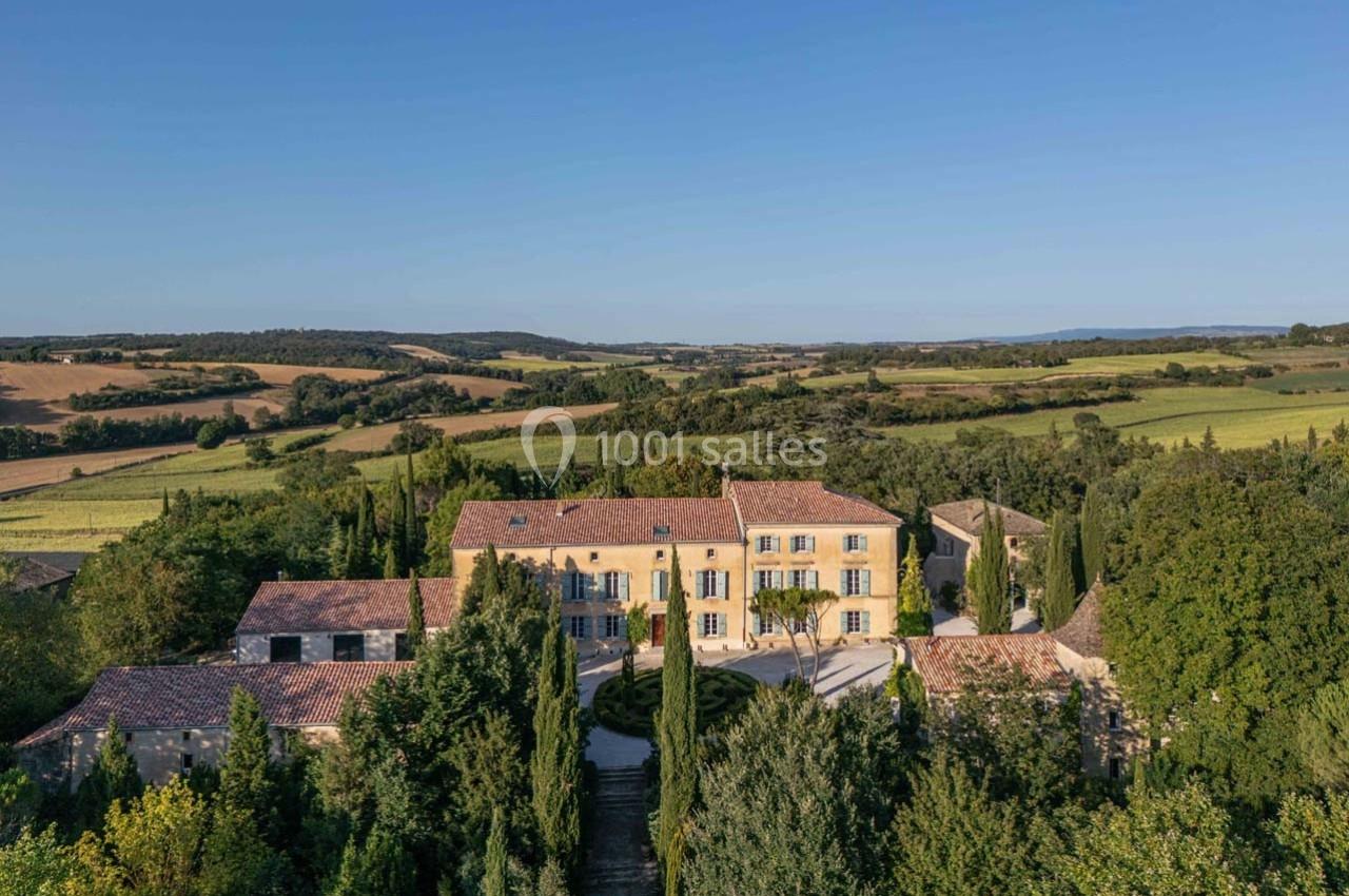 Vue aérienne d'un grand domaine provençal entouré de champs, d'arbres et de collines sous un ciel dégagé.