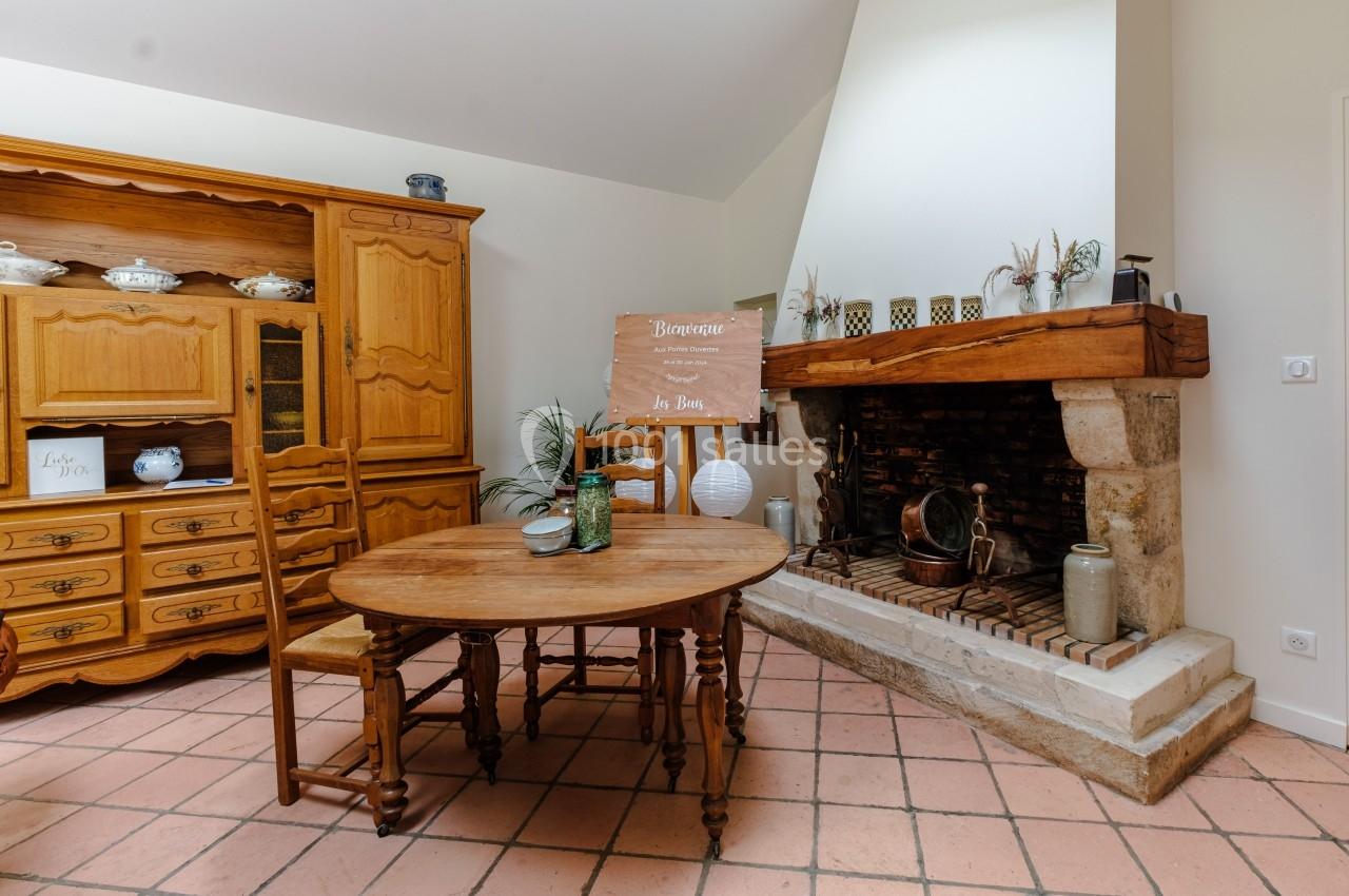 Salle à manger rustique avec table en bois, cheminée en pierre et vaisselier en arrière-plan.