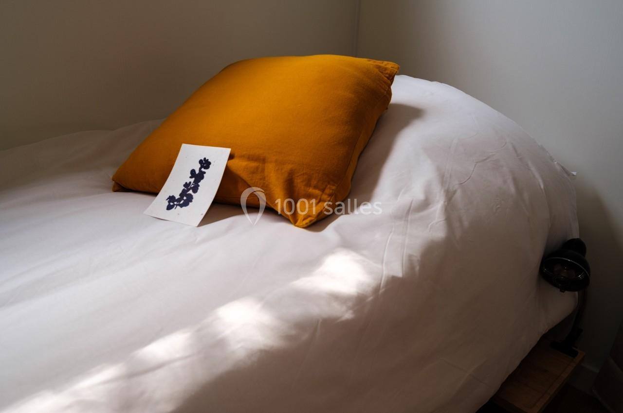 Oreiller jaune sur un lit blanc avec une carte illustrée posée dessus, éclairé par une lumière naturelle.