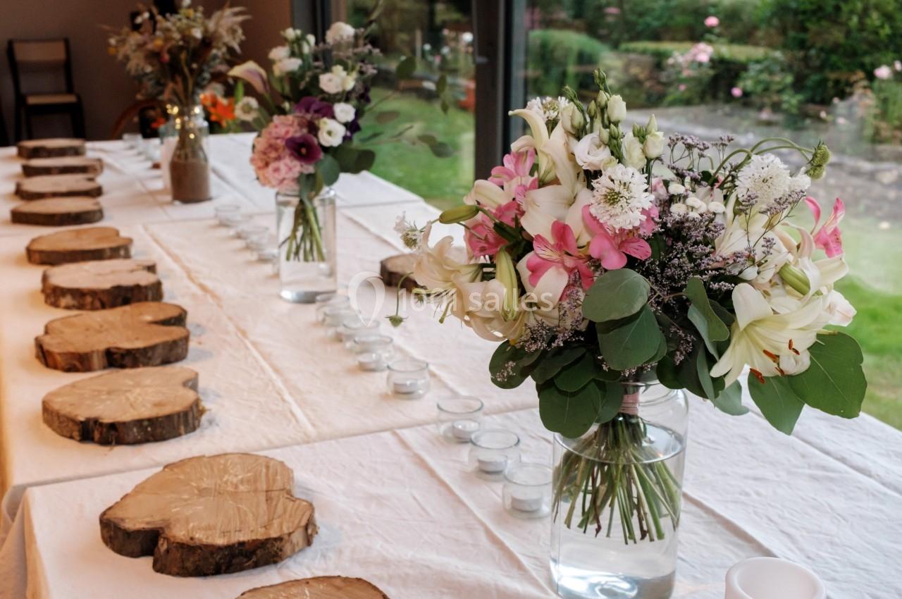 Table décorée avec des rondins de bois, des bougies et des bouquets de fleurs dans des vases en verre, près d'une baie…