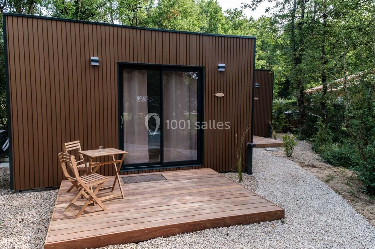 Petite terrasse en bois avec table et chaises devant une maison moderne en bois, entourée de végétation.