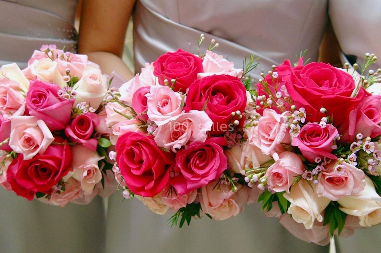 Bouquets de roses rouges et roses tenus par des personnes en robes pastel.
