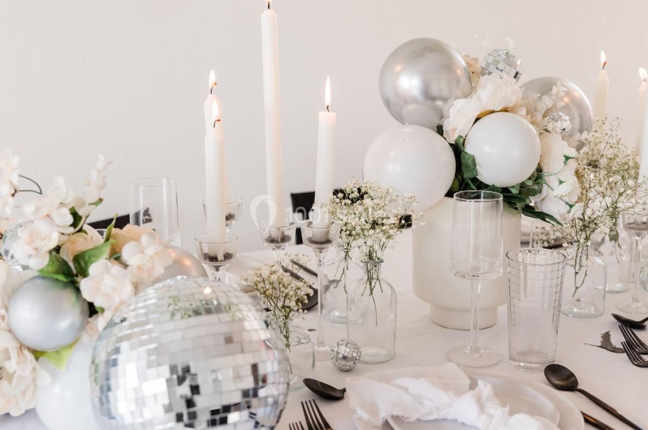 Table décorée avec des bougies blanches, des fleurs, des ballons argentés et une boule à facettes.