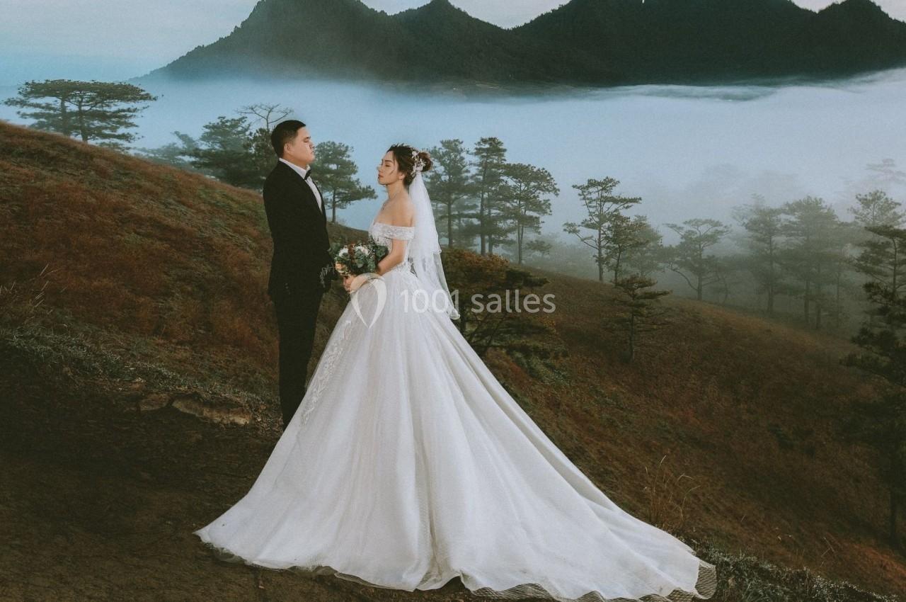 Un couple en tenue de mariage se tient sur une colline brumeuse avec des montagnes en arrière-plan.