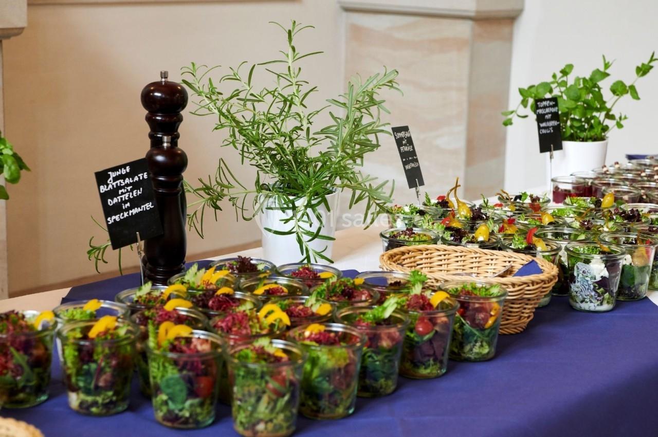 Buffet avec des salades colorées en verrines, herbes fraîches en pots et moulin à poivre sur une nappe bleue.