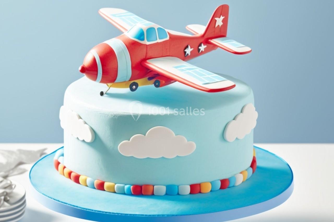 Gâteau bleu décoré de nuages avec un avion rouge en sucre posé sur le dessus.