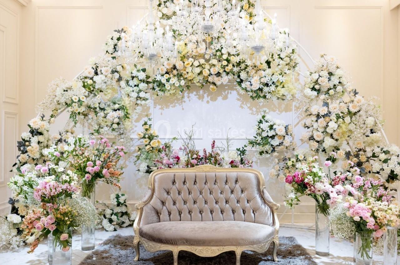 Canapé beige devant une arche ornée de fleurs blanches et colorées dans un décor lumineux et élégant.