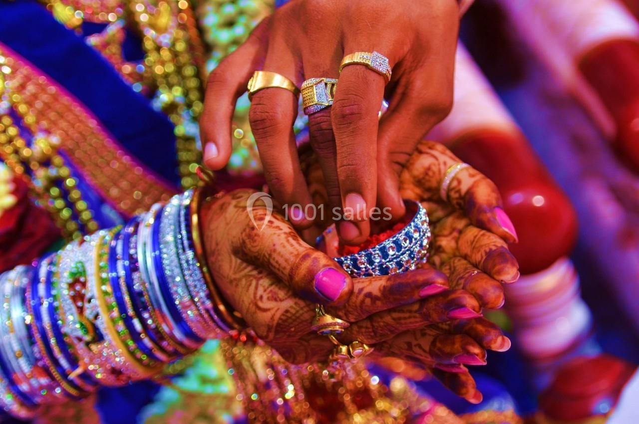 Deux mains ornées de bijoux et de henné tiennent un bracelet coloré dans un contexte de cérémonie festive.
