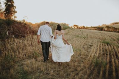 Miniature Event&co Art'gency #41 Un couple marche dans un champ au coucher du soleil, la femme portant une robe blanche et tenant légèrement son ourlet.