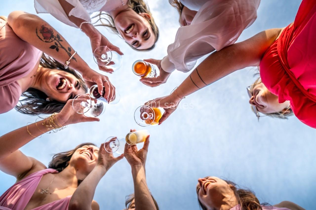 Personnes souriantes levant des verres pour un toast, vues en contre-plongée sous un ciel bleu.