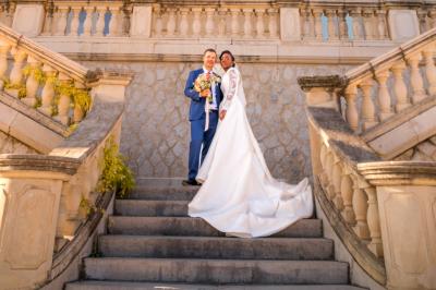 Femme en robe blanche souriante, assise près d'une fontaine, avec un homme en costume visible de dos.