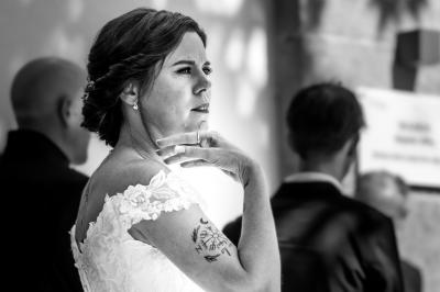 Femme en robe blanche souriante, assise près d'une fontaine, avec un homme en costume visible de dos.