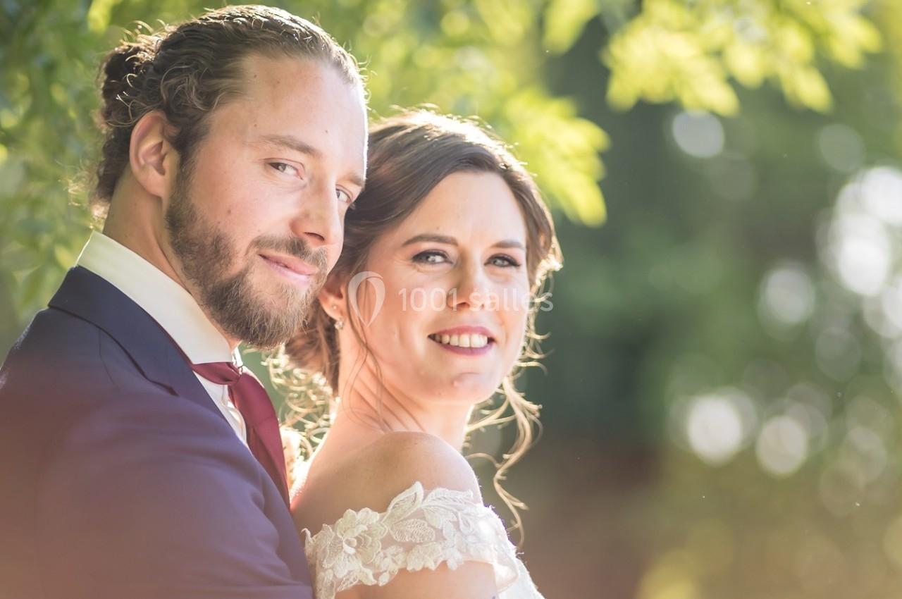Un couple souriant en tenue de mariage, posé dans un cadre extérieur lumineux avec un arrière-plan verdoyant.