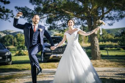 Femme en robe blanche souriante, assise près d'une fontaine, avec un homme en costume visible de dos.