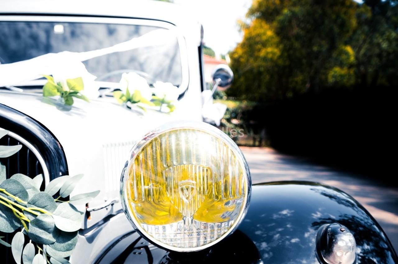 Gros plan sur le phare avant d'une voiture ancienne décorée de fleurs pour un événement festif, en extérieur.