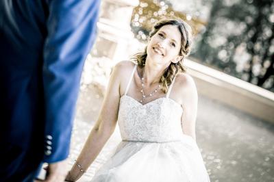 Femme en robe blanche souriante, assise près d'une fontaine, avec un homme en costume visible de dos.