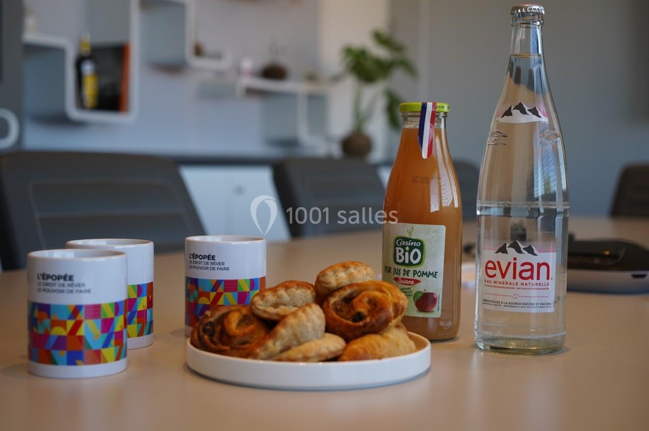 Assortiment de viennoiseries sur une table avec des tasses, une bouteille de jus de pomme et une bouteille d'eau.