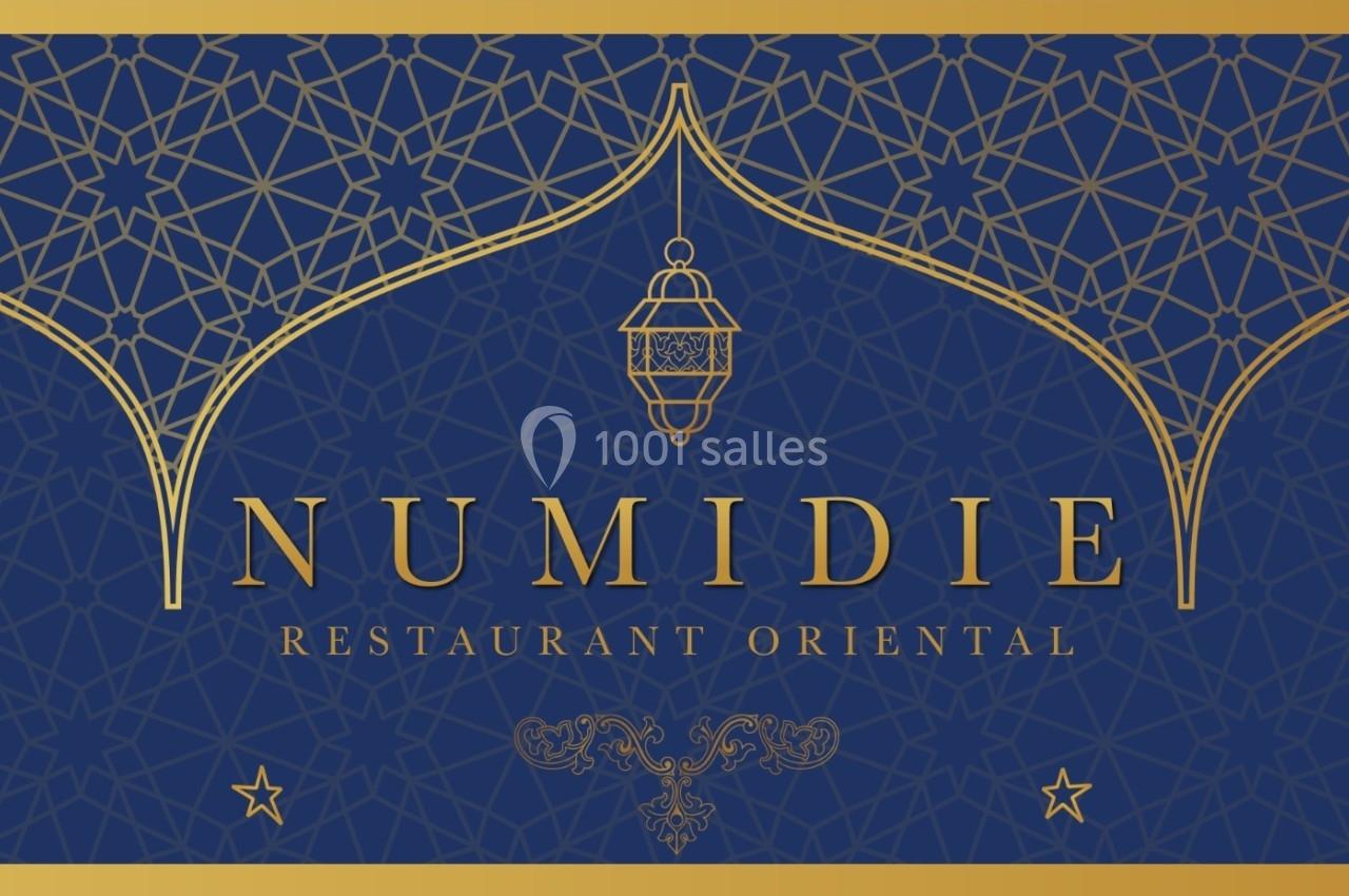 Motif oriental doré sur fond bleu avec le texte ’Numidie Restaurant Oriental’ et une lanterne décorative au centre.