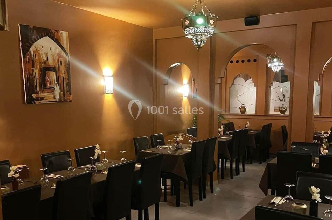 Salle de restaurant chaleureuse avec murs ocres, tables dressées, chaises noires et luminaires suspendus.