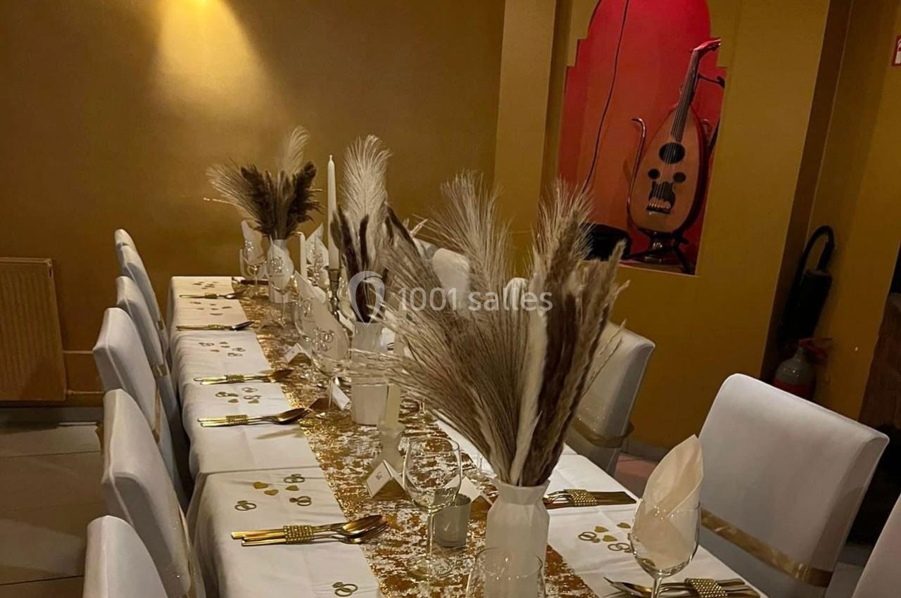 Table dressée avec nappes blanches, décorations dorées, vases de pampas et fond avec un oud exposé.