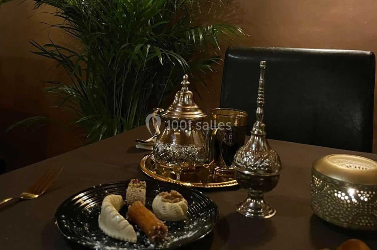 Table dressée avec des pâtisseries orientales, une théière en métal, un verre à thé et des objets décoratifs.