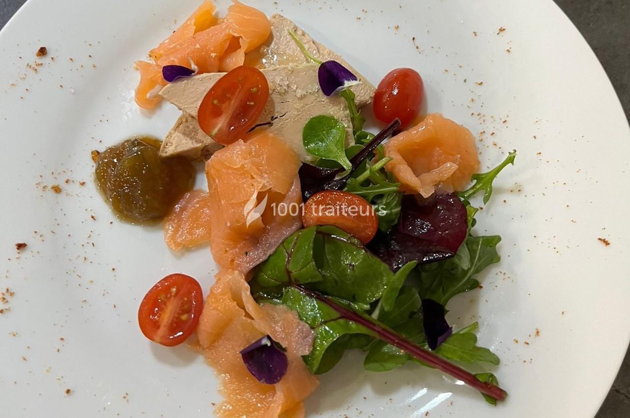 Assiette garnie de saumon fumé, foie gras, salade verte, tomates cerises et chutney, présentée sur une assiette blanche.
