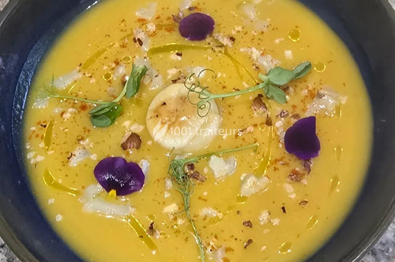 Soupe de légumes jaune garnie de fleurs comestibles, herbes fraîches, noix concassées et filet d'huile.