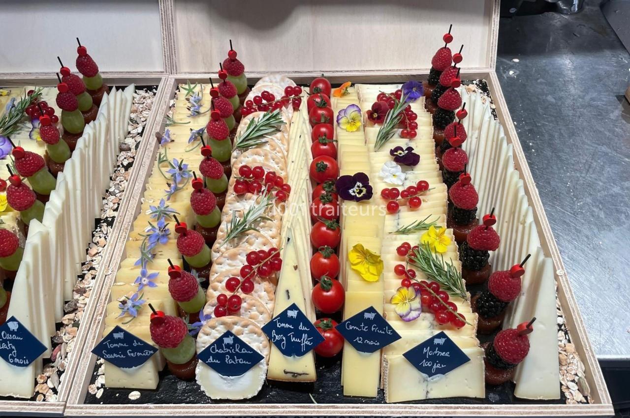 Plateau de fromages variés décoré de fruits rouges, herbes aromatiques et fleurs comestibles, présenté dans une boîte en…