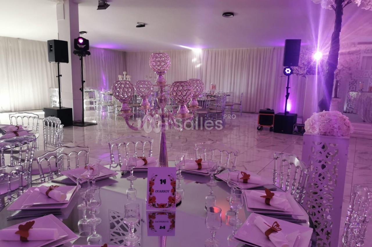 Salle de réception dressée pour banquet avec éclairage violet, tables décorées et candélabres en cristal.