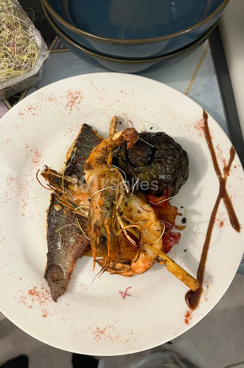 Assiette blanche avec filet de poisson, crevettes et légumes grillés, sauce rouille et poudre de paprika.