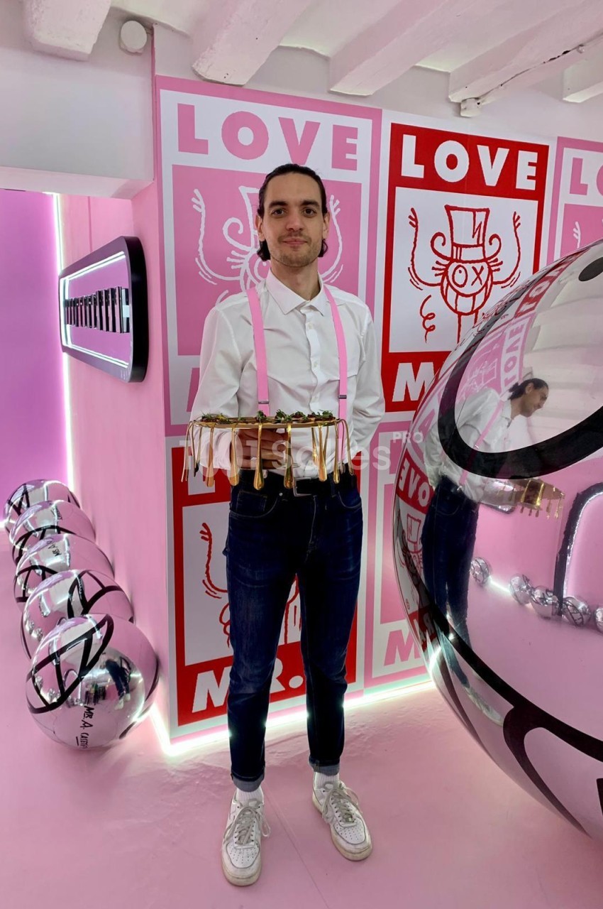 Homme tenant un plateau de mignardises dans un espace rose aux néons et panneaux LOVE.