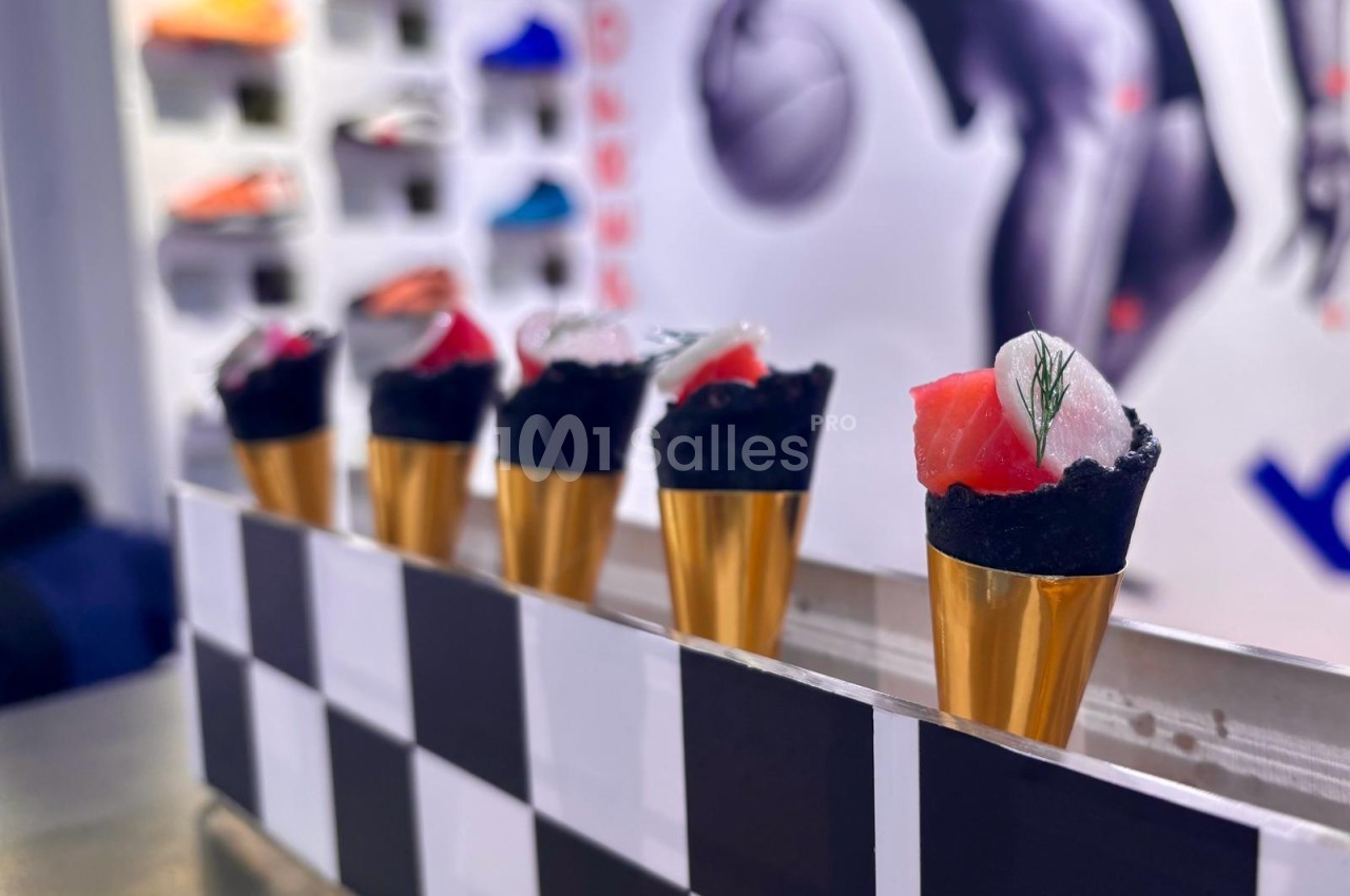 Canapés miniatures en verre doré avec garnitures noires et rouges alignés sur un plateau à damier.