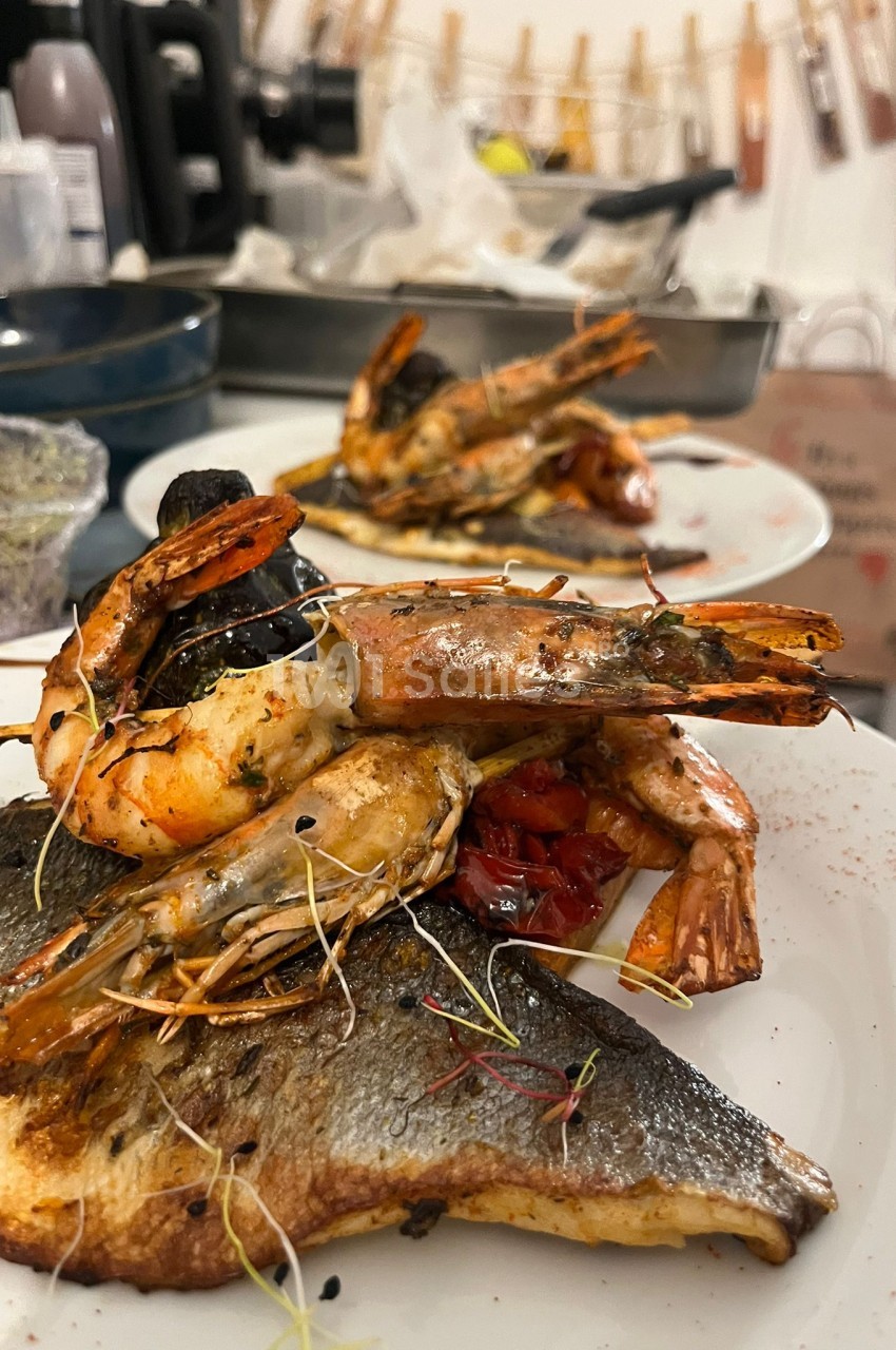 Langoustines et filet de poisson grillés garnis d'herbes, dressés en assiette de cuisine professionnelle.