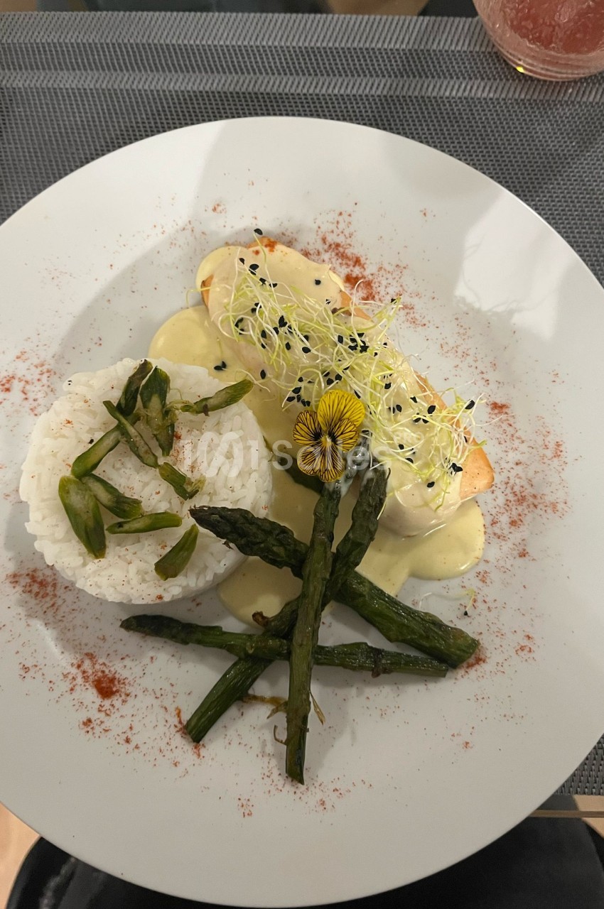 Assiette blanche avec filet de poisson, purée, asperges, microgermes et fleur comestible saupoudrée de paprika.