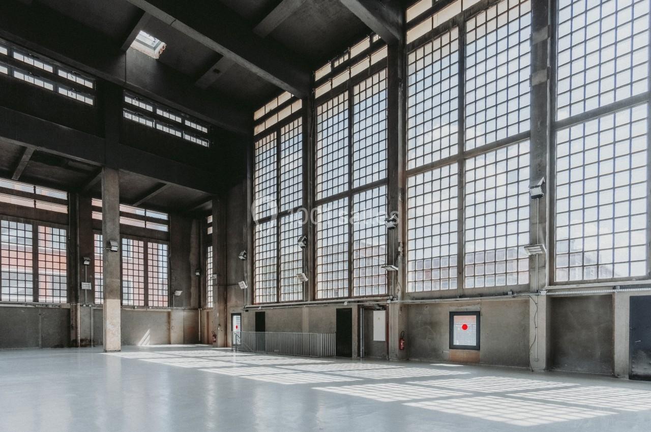 Intérieur d'un grand bâtiment industriel avec de hautes fenêtres à carreaux laissant entrer une lumière naturelle.