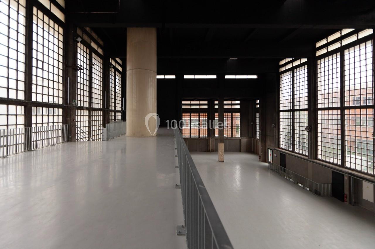 Intérieur d'un bâtiment industriel avec de grandes fenêtres en grille et un espace ouvert au sol clair.
