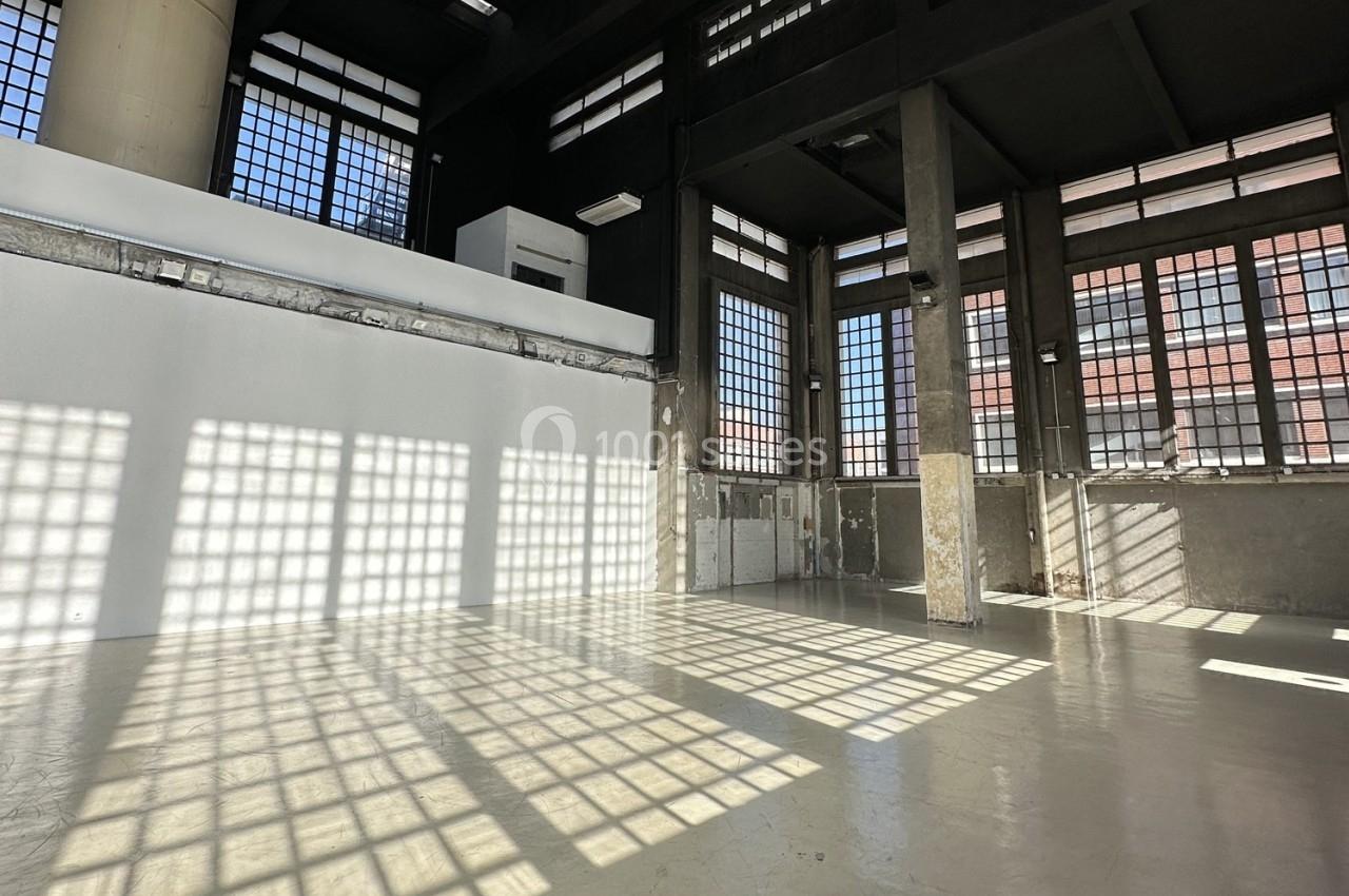 Intérieur d'un grand espace industriel avec des murs en béton, des colonnes et de grandes fenêtres laissant entrer la…