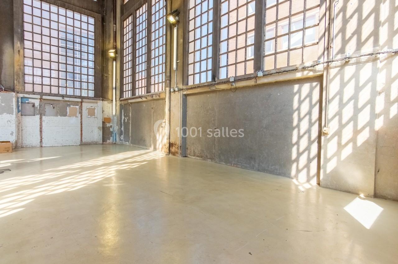 Intérieur d'un grand espace industriel vide avec sol en béton, murs en béton brut et larges fenêtres laissant entrer la…