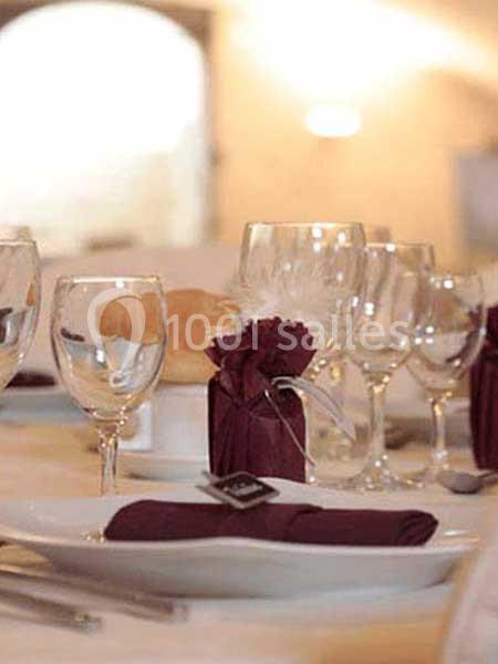 Table dressée avec des verres à pied, serviettes pliées et décoration en tissu bordeaux, ambiance élégante.