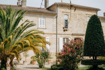 Miniature Location salle Margaux (Gironde) - Château Pontac Lynch #2 Femme de dos, vêtue d'un chapeau et d'une tenue claire, levant un verre de vin devant une façade en pierre avec volets…