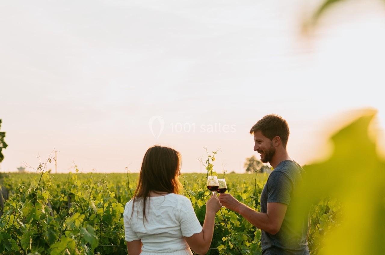 Un homme et une femme trinquent avec des verres de vin dans un vignoble au coucher du soleil.